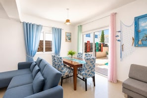 A living room with a sofa, dining table, chairs, and a small table with a plant. - Villa Chromata - Three Bedroom Villa, Sleeps 7 (Pernera)