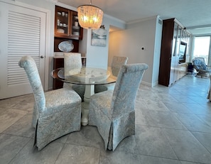 A dining area with a round glass table, upholstered chairs, a chandelier, and a view of the outdoors. - Sabine 3D Waterfront Bay Views Sleeps 6 (Pensacola Beach)