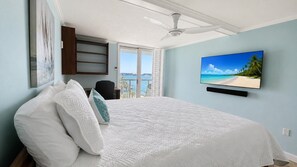 Um quarto com uma cama, uma televisão na parede e vista para o mar.