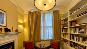 A cozy reading room with two armchairs, a fireplace, and a bookshelf filled with books. - Stunning Family Home in Tulse Hill (London)