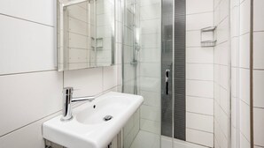 Une salle de bain moderne avec un lavabo blanc, une douche en verre et un grand miroir.