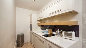 Une cuisine compacte avec des meubles blancs, une poubelle en acier inoxydable, un grille-pain et une bouilloire.