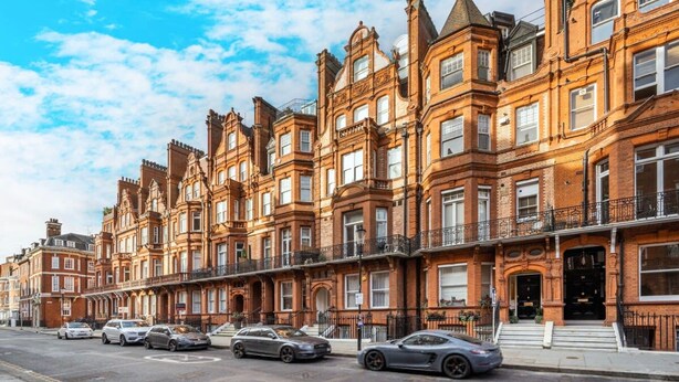 Une rangée de maisons de ville aux façades en briques rouges, à plusieurs étages, dotées de grandes fenêtres et d’un style architectural classique.
