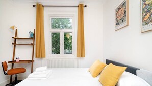 A hotel room with a bed, a desk with a chair, a window with curtains, and artwork on the wall. - Chic One-Bedroom Apartment in London (London)
