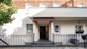 Une maison de ville avec une entrée à l’avant, un petit porche et un bâtiment en briques en arrière-plan.