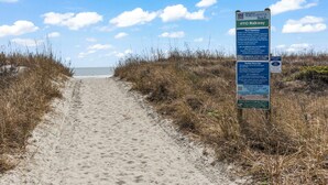 Un camí de sorra amb un senyal que indica el passeig marítim 4910 i les normes de la platja.