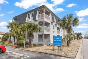 A multi-story building with balconies, palm trees, and a sign indicating it's a place at the beach. - Ocean & Inlet Views | Cherry Grove Condo (North Myrtle Beach)