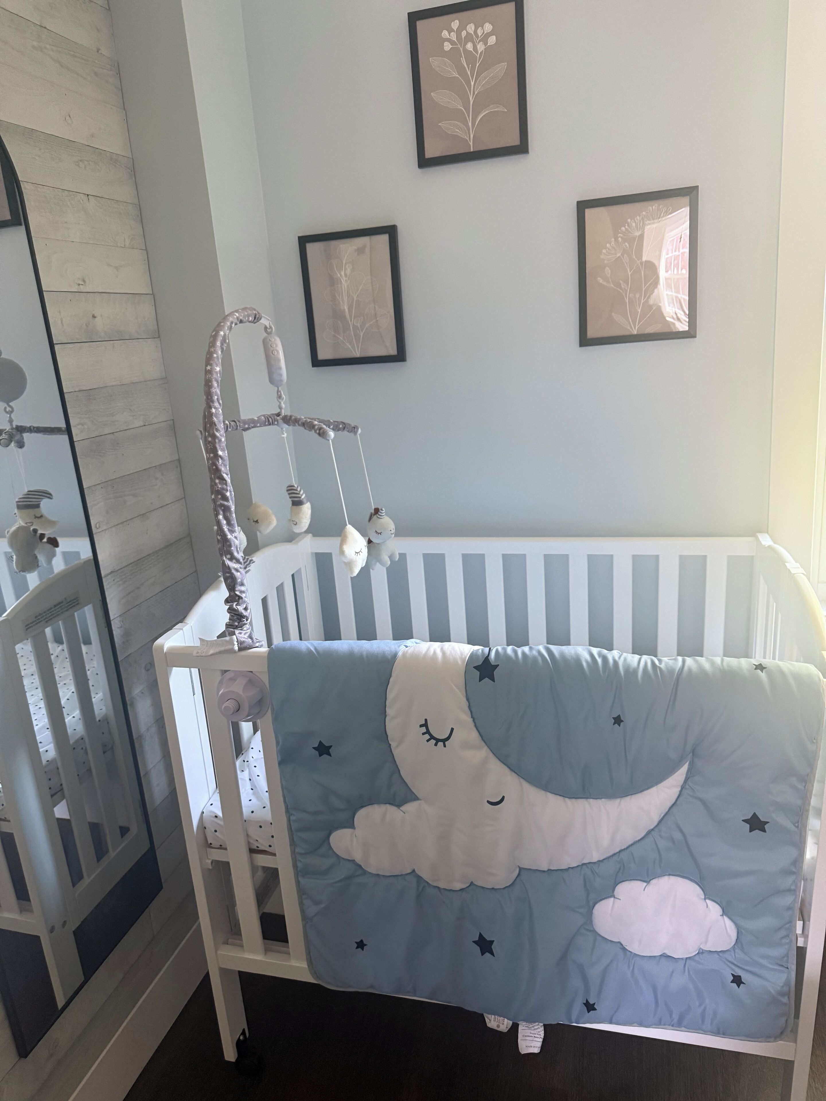 Een babybedje met een blauw-wit gestreept matras, een ontwerp van een maan en wolken, en een hangende mobiel.