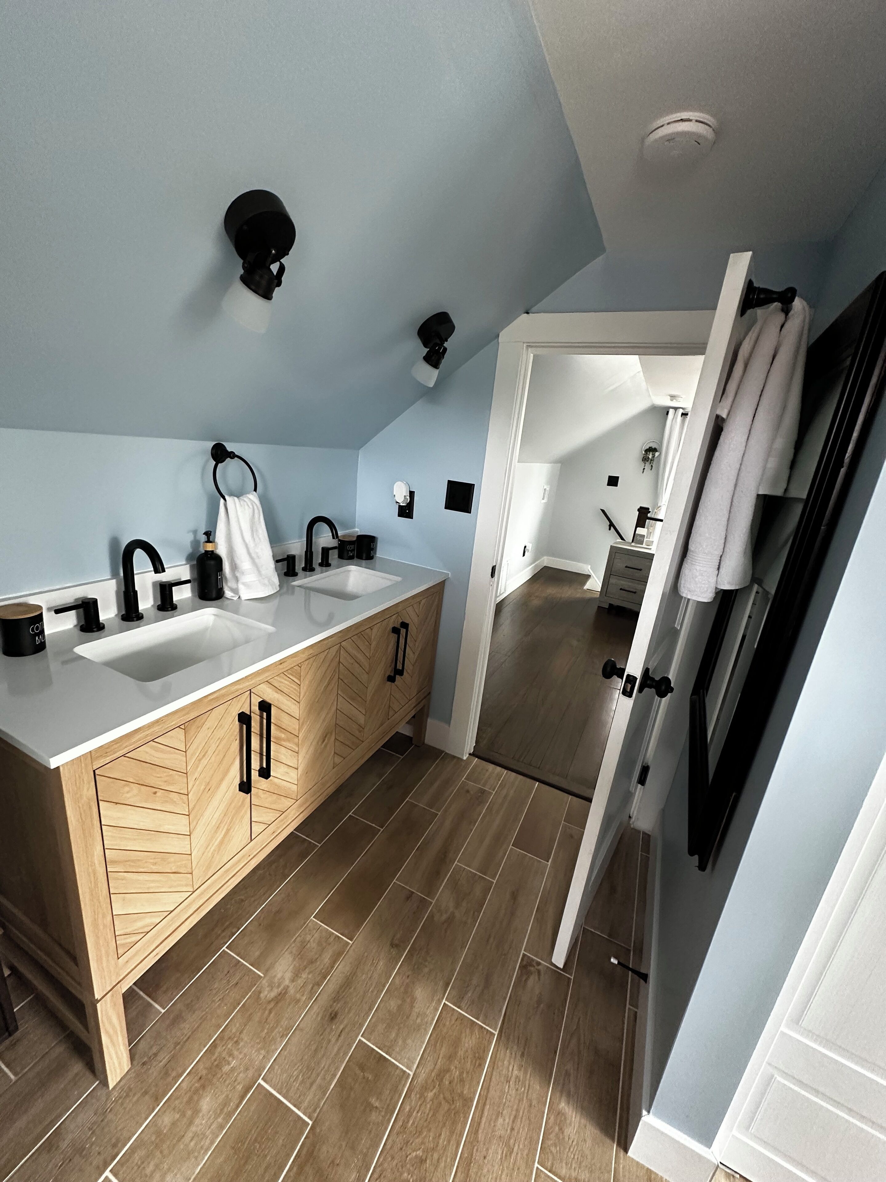 Une salle de bain moderne avec un meuble-lavabo à deux vasques, des armoires en bois et un sol décoré d’un motif en chevrons.