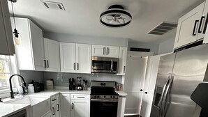 A modern kitchen with white cabinets, stainless steel appliances, and a wooden floor. - Charming 3-bedroom completely remodeled country house in Tappahannock with AC (Tappahannock)