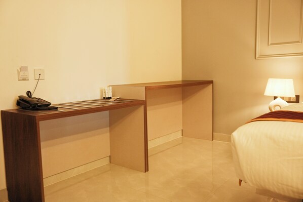 A hotel room with a wooden desk, a telephone, a lamp, and a bed. - Hemagiri Palace (Devanahalli)