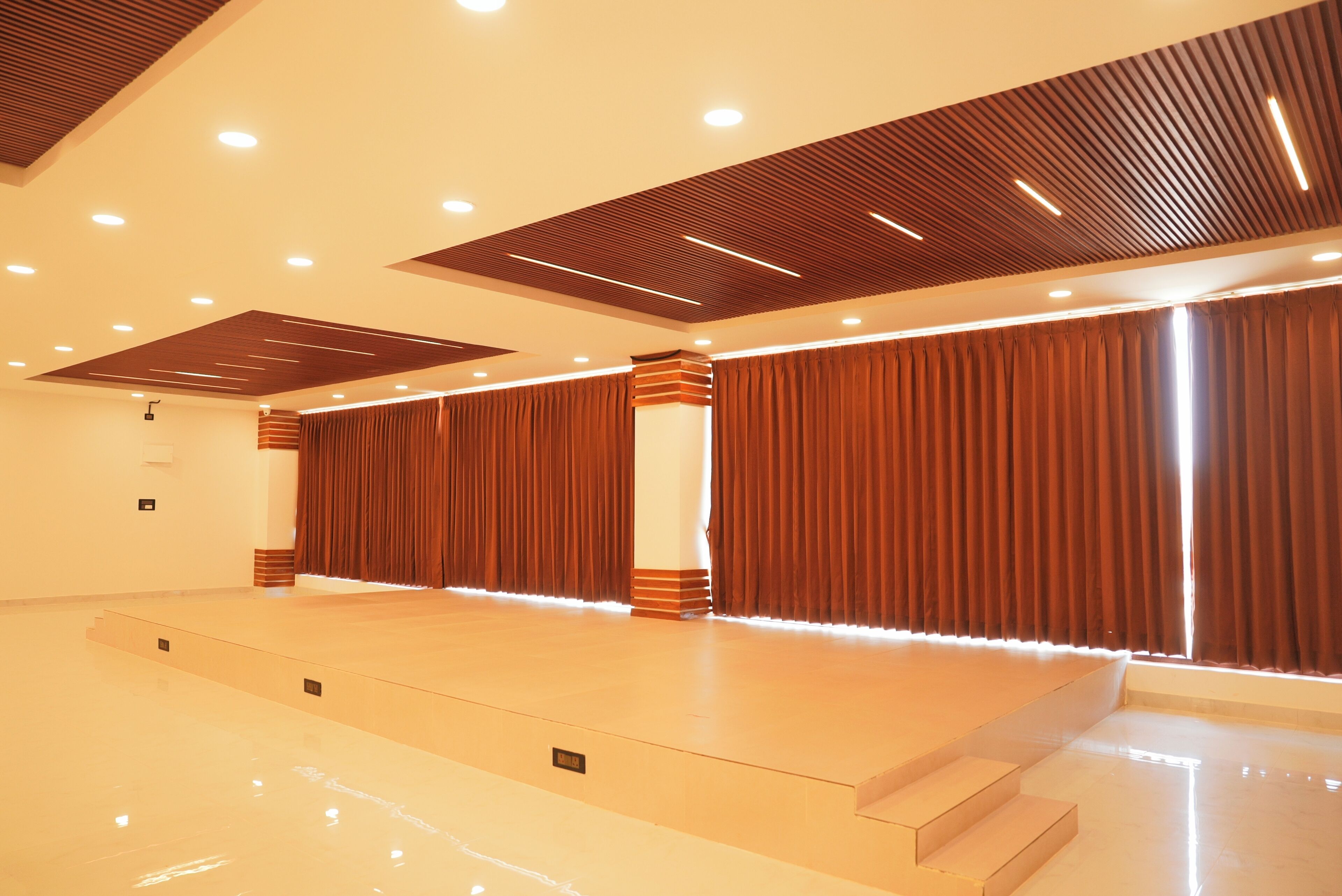 A spacious hall with a stage, tiered seating, and a modern ceiling design.