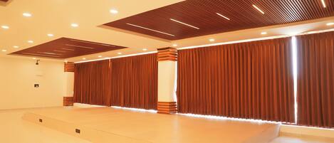 A spacious hall with a stage, tiered seating, and a modern ceiling design.