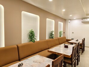 A modern dining area with a long brown bench, marble-topped tables, and wooden chairs. - Hemagiri Palace (Devanahalli)