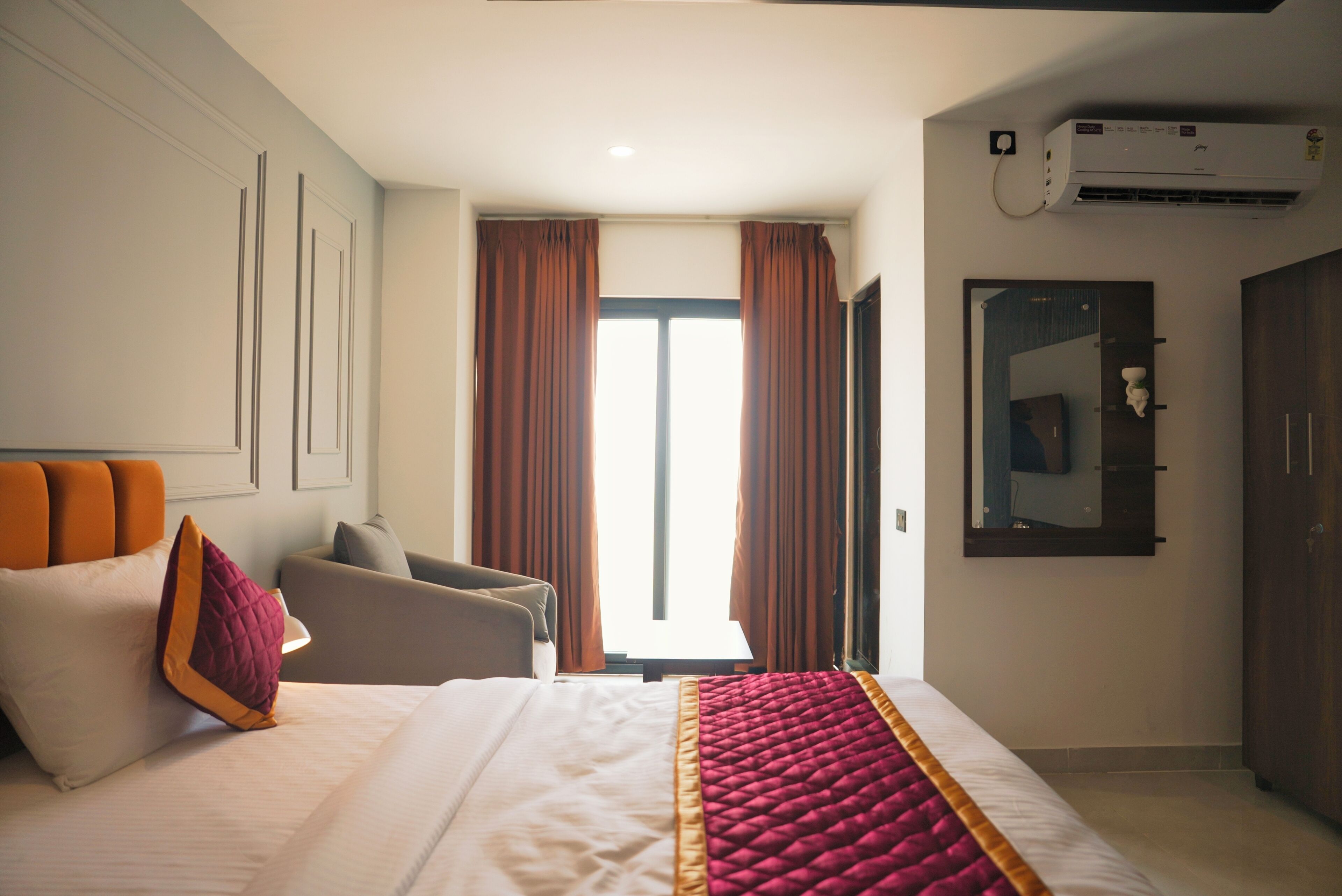 Een hotelkamer met een bed, een stoel, een bureau, een airconditioner en een spiegel aan de muur.