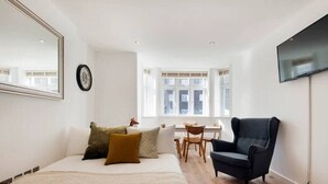 Un dormitorio con cama, una silla, televisión y ventana que deja entrar luz natural.