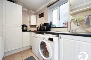 Een kleine keuken met een ingebouwde wasmachine, een koffiezetapparaat en een spoelbak.