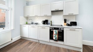 A modern kitchen with white cabinets, a built-in oven, and a window with blinds. - Serene One-Bedroom Retreat in Fitzrovia (London)