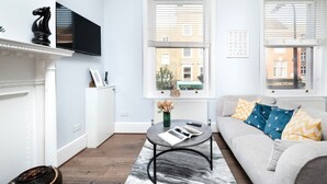 A modern living room with a fireplace, a mounted TV, a sofa with patterned cushions, and a round coffee table. - Serene One-Bedroom Retreat in Fitzrovia (London)