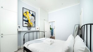 A bedroom with a bed, white walls, a ceiling light, and a door leading to another room. - Serene One-Bedroom Retreat in Fitzrovia (London)