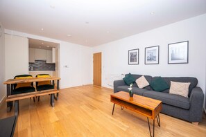 A modern living room with a grey sofa, wooden coffee table, and a dining area with a wooden table and chairs.