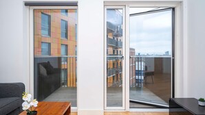 A modern apartment with a sliding glass door leading to a balcony, a grey sofa, and a wooden coffee table with a potted orchid.
