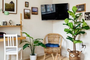 A room with a desk, chair, potted plants, a television, and framed pictures on the wall. - Luxury Studio in Heart of Richmond (Greater London)