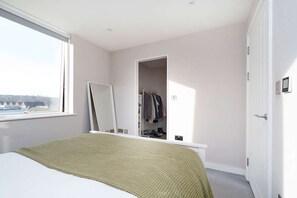 Un dormitorio con cama, ventana grande, armario y espejo.