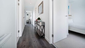 Ein Gang mit Holzboden, weißen Wänden und einem Bett mit weißer Bettwäsche im Zimmer.