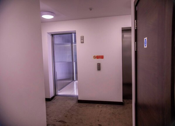 A hallway with an elevator, a door with a blue accessibility symbol, and a sign indicating elevator use during fire events.
