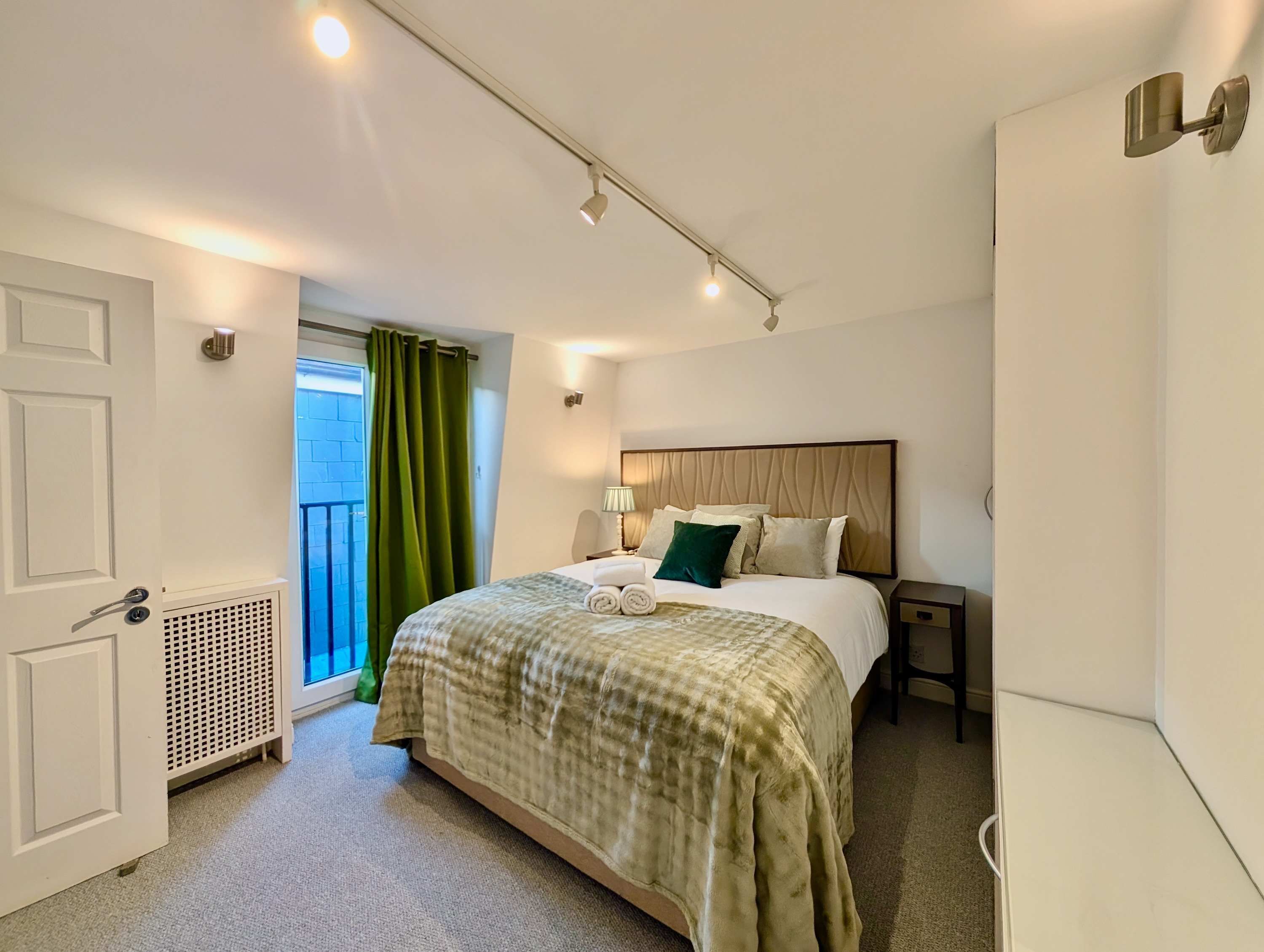 A hotel room with a bed, a nightstand, a lamp, a window with curtains, and a radiator.
