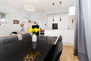 A modern living room with a black dining table, a sofa, and a coffee table with yellow flowers. There is a kitchen area with a stove and a sink. - Charming Ground Floor Flat in Twickenham (Twickenham)