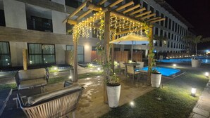 Une terrasse extérieure dotée d’une pergola, de sièges, d’une piscine et de plantes en pot.
