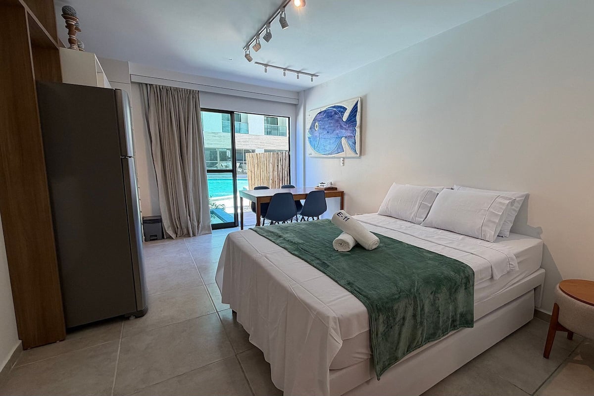 A hotel room with a bed, a desk, a chair, a small table, and a view of the ocean.