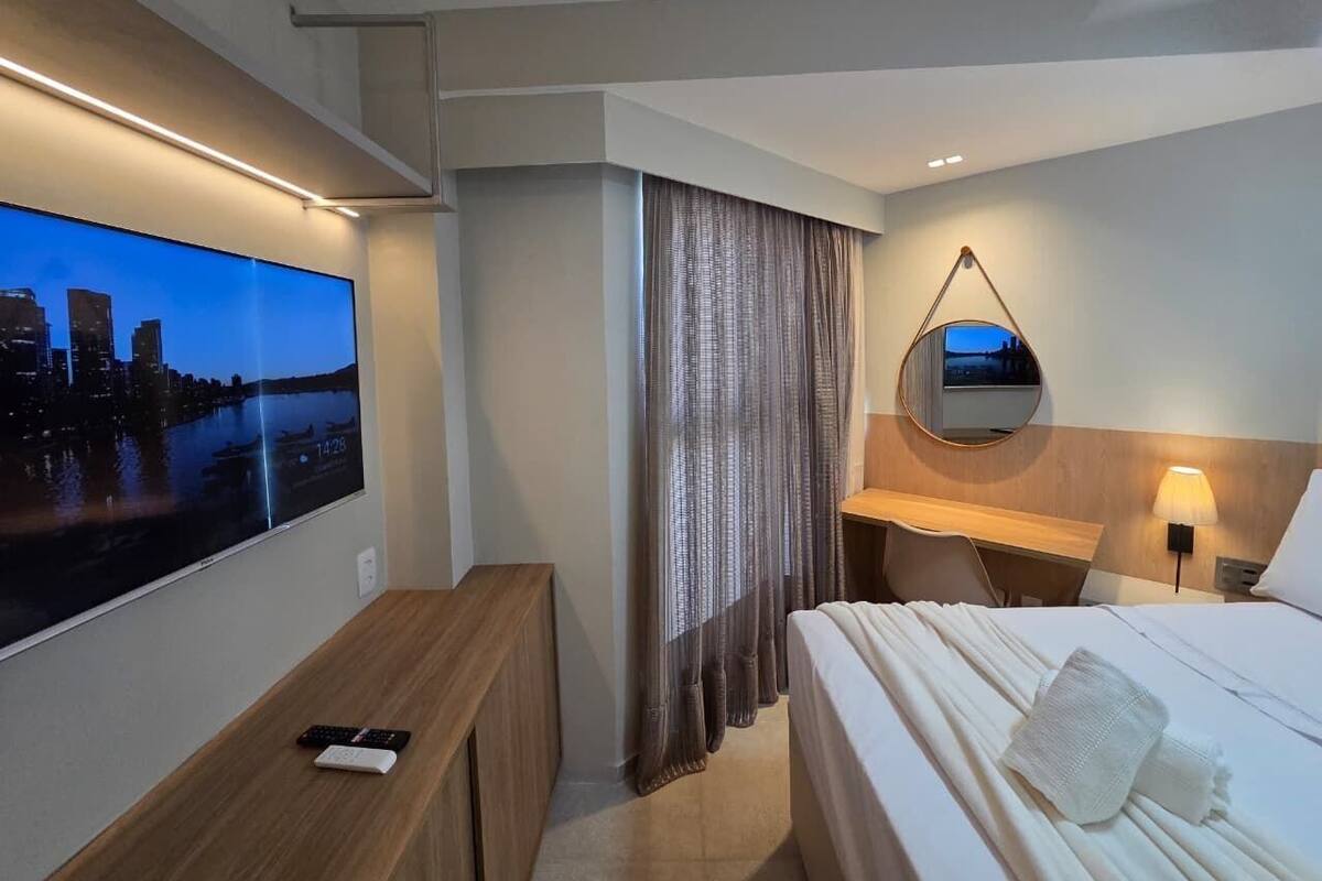A hotel room with a bed, a desk, a TV, a mirror, and curtains.