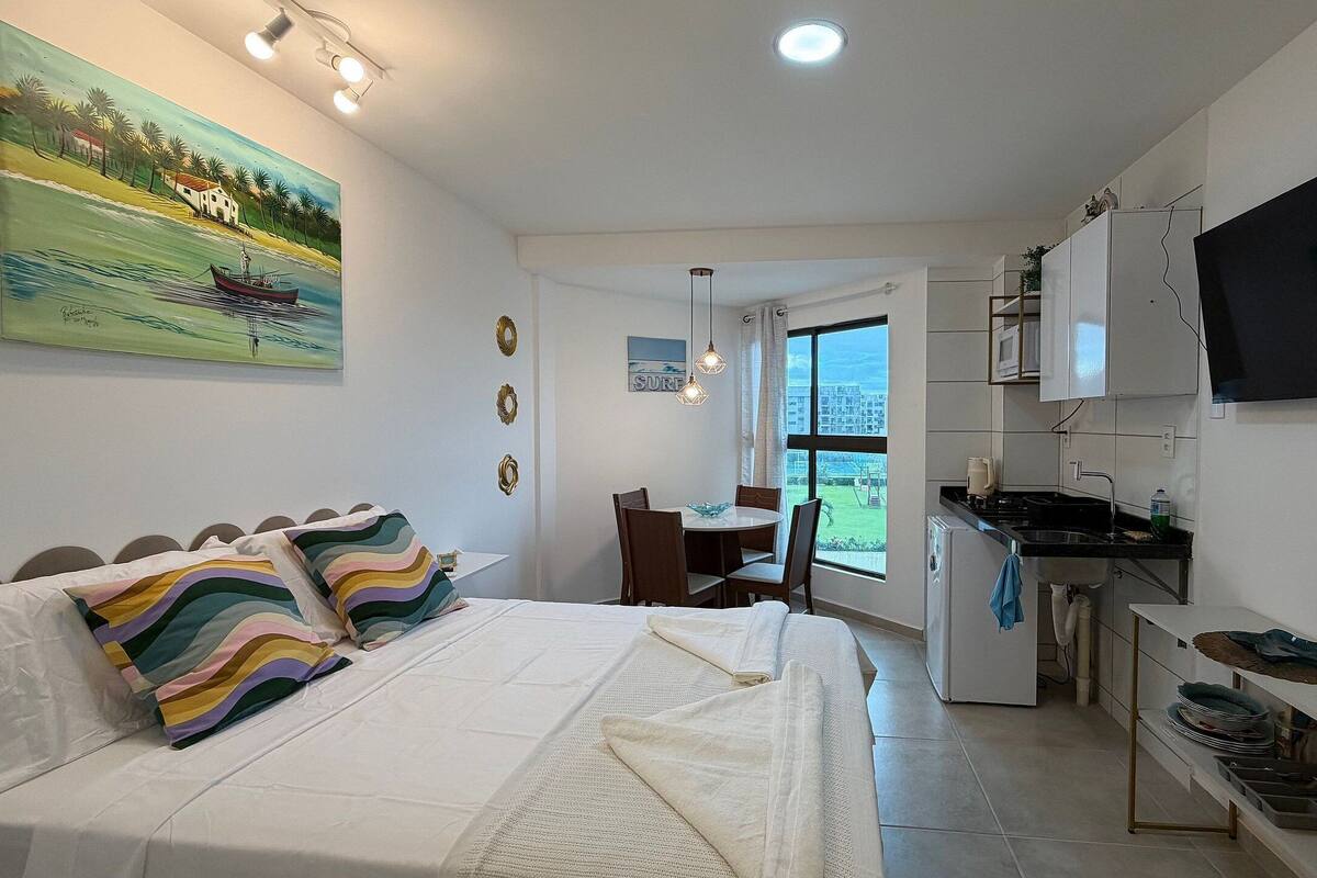 A bedroom with a bed, a dining table, and a kitchen area with a TV.