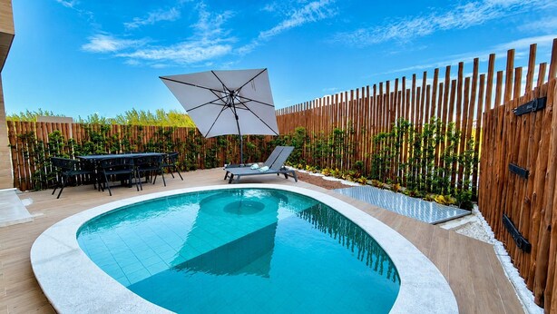 Une piscine entourée d’une clôture en bois, avec des chaises longues et une table avec des chaises.