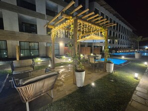 An outdoor patio with a pergola, seating, a pool, and potted plants. - Max Carneiros (Tamandaré)