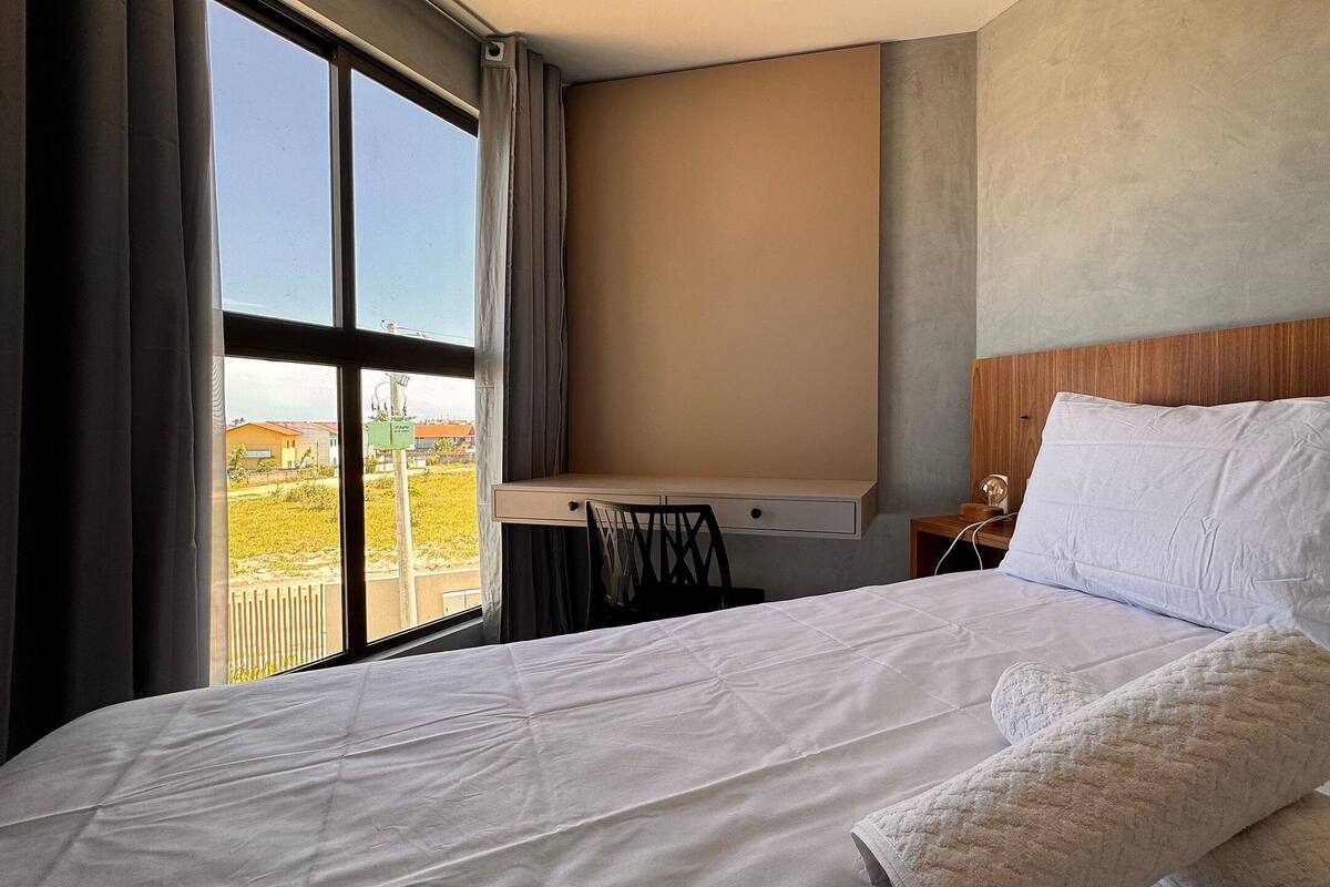 A hotel room with a large bed, a wooden headboard, a nightstand, and a view of a building through a window.