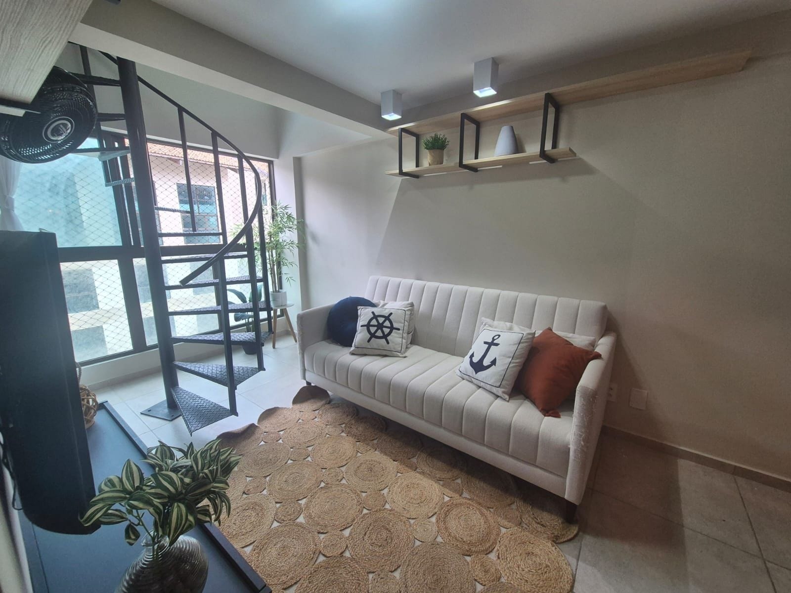 Una sala de estar con un sofá, un tapete estampado, una escalera y una estantería con adornos.