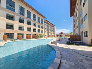 A swimming pool surrounded by a building with multiple balconies and a clear sky. - Max Carneiros (Tamandaré)