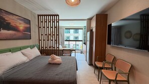 A hotel room with a bed, a desk, chairs, a TV, and a view of the city. - Max Carneiros (Tamandaré)
