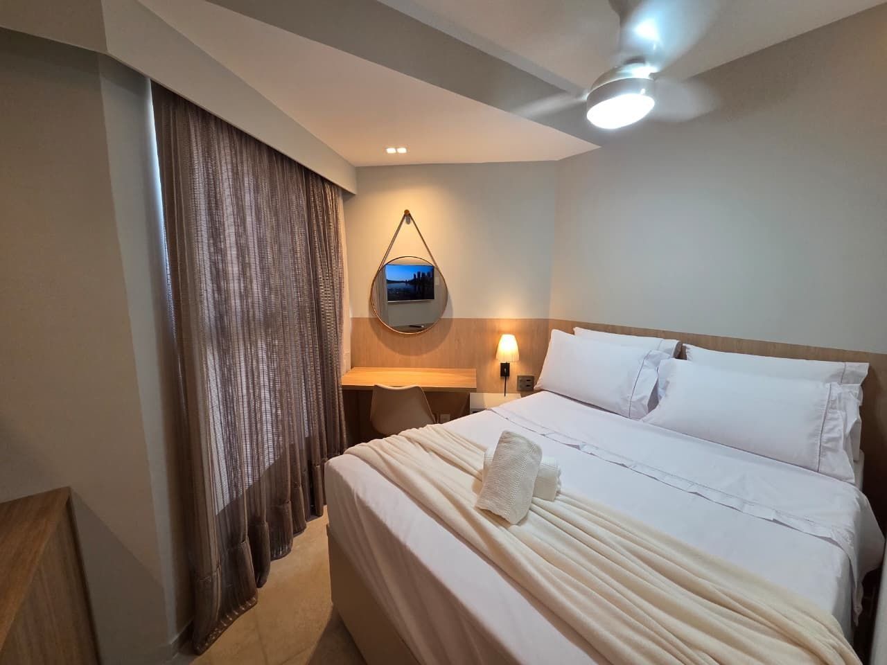 A hotel room with a bed, a desk, a chair, a TV, and a ceiling fan.