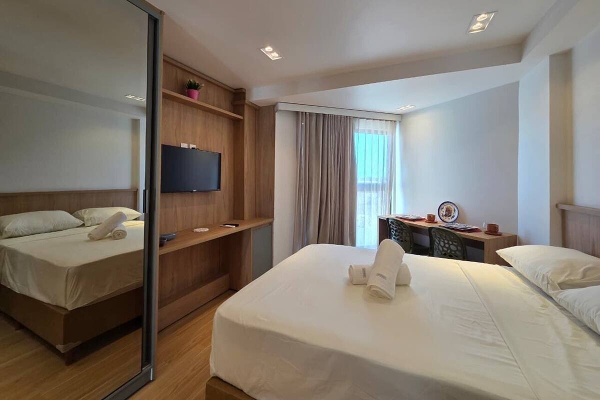 A hotel room with a bed, a TV, a desk, and a window with curtains.