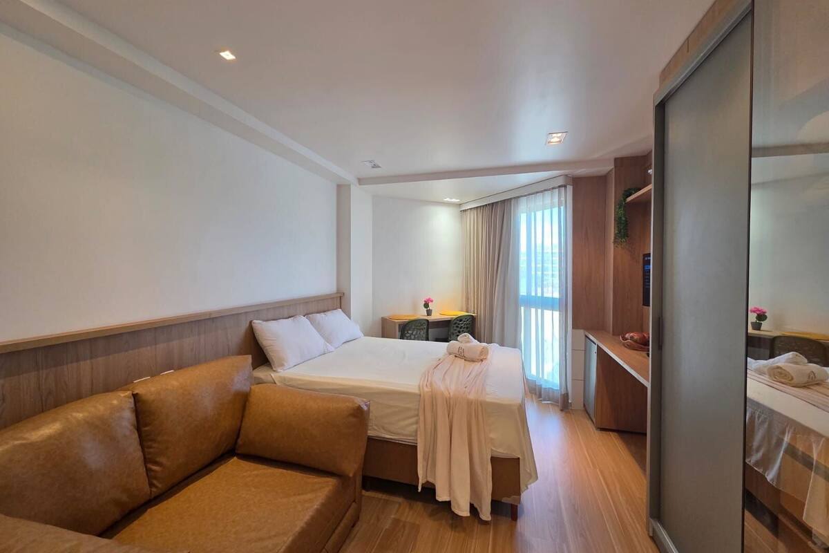 A hotel room with a bed, a sofa, a desk, and a large window with curtains.