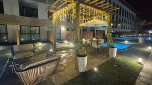 An outdoor patio with a pergola, seating, a pool, and potted plants. - Max Carneiros (Tamandaré)