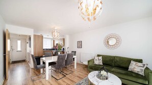 A modern living room with a green sofa, a white coffee table, and a dining area with a white table and grey chairs. - Charming 2-Bedroom House in Northfleet (Northfleet)