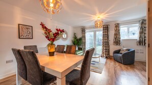 A modern dining area with a wooden table and chairs, a vase of flowers, and a chandelier. - Charming 2-Bedroom House in Northfleet (Northfleet)