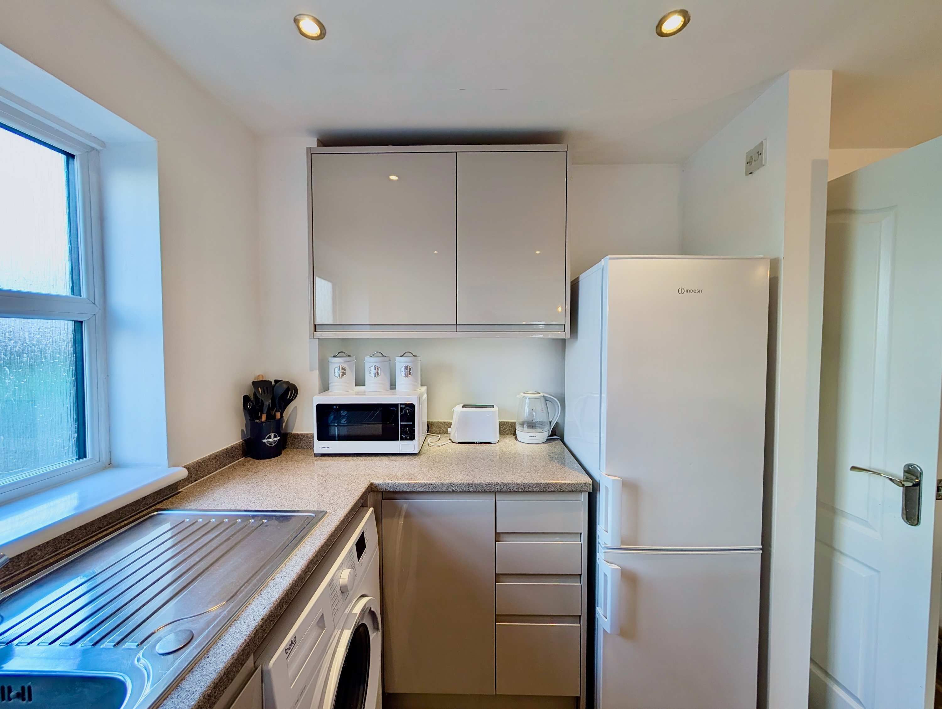 A compact kitchen with a washing machine, microwave, toaster, and refrigerator.
