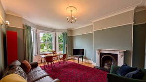 A living room with a fireplace, a sofa, a TV, and a dining area with a table and chairs. - Charming Two-Bedroom House in London (Greater London)